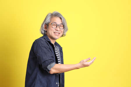 The senior Asian man with jean dressed standing against the yellow background.の写真素材