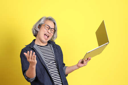 The senior Asian man with jean dressed standing against the yellow background.の写真素材