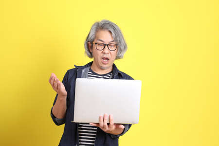 The senior Asian man with jean dressed standing against the yellow background.の写真素材