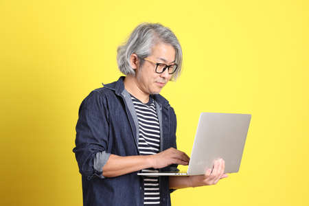 The senior Asian man with jean dressed standing against the yellow background.の写真素材