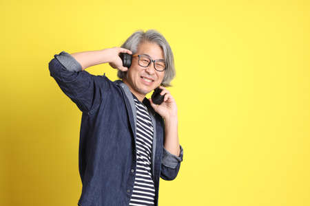 The senior Asian man with jean dressed standing against the yellow background.の写真素材