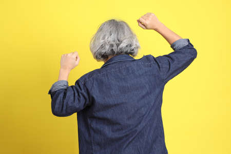 The senior Asian man with jean dressed standing against the yellow background.の写真素材