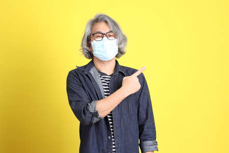 The senior Asian man with jean dressed standing against the yellow background.の写真素材