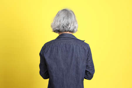 The senior Asian man with jean dressed standing against the yellow background.の写真素材