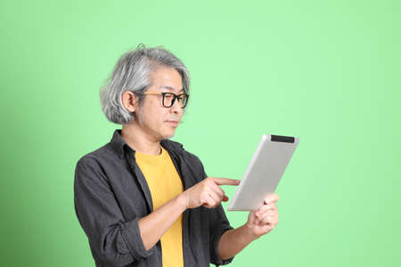 The senior Asian man with smart casual dressed standing against the light green background.