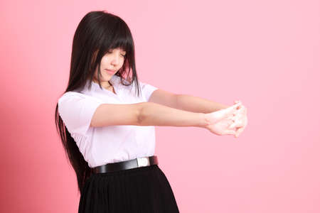 The teen Asian girl with university uniform standing on the pink background.