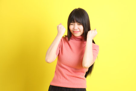 The teen Asian girl with casual dressed standing on the yellow background.の写真素材