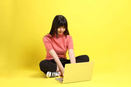 The teen Asian girl with casual dressed sitting on the yellow background.の写真素材