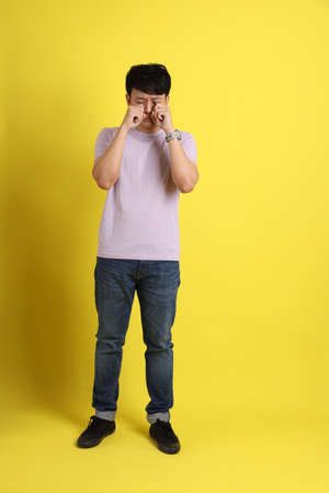 The young adult Asian man standing on the yellow background.