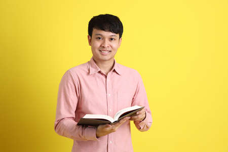 The young adult Asian man standing on the yellow background.
