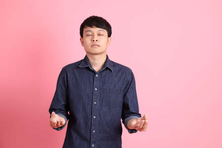The young adult Asian man standing on the pink background.の写真素材