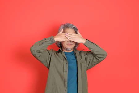 The senior Asian man with casual clothes standing on the orange background.