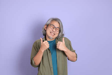 The senior Asian man with casual clothes standing on the purple background.の写真素材
