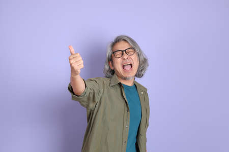 The senior Asian man with casual clothes standing on the purple background.の写真素材
