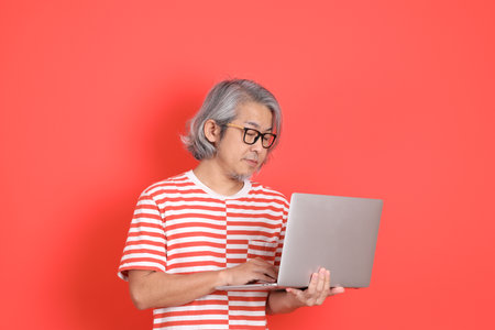 The senior Asian man with casual clothes standing on the orange background.の写真素材