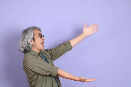The senior Asian man with casual clothes standing on the purple background.の写真素材