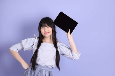 The young Asian girl in purple preppy dressed standing on the purple background.