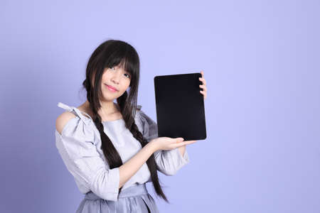 The young Asian girl in purple preppy dressed standing on the purple background.の写真素材