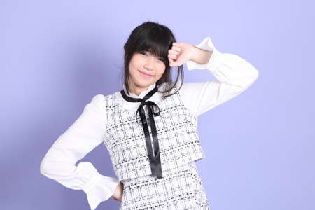 The young Asian girl in white preppy dressed standing on the purple background.