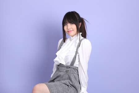 The cute young Asian girl with white preppy dressed style sitting on the purple background