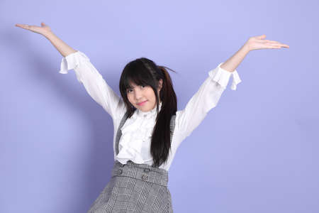 The cute young Asian girl with white preppy dressed style sitting on the purple backgroundの写真素材