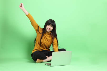 The young Asian girl in casual dressed sitting on the green background.の写真素材