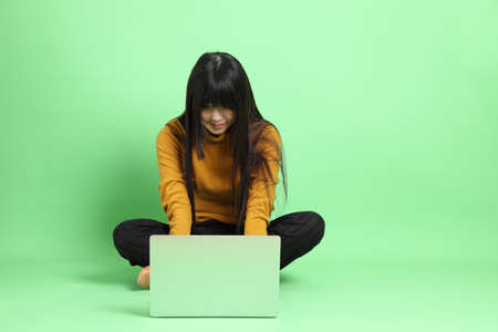 The young Asian girl in casual dressed sitting on the green background.の写真素材