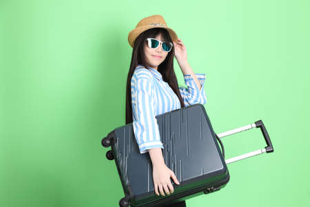 The young Asian girl in casual dressed standing on the green background with luggage.の写真素材