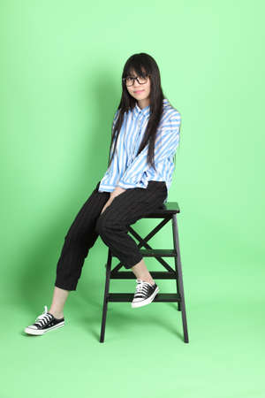 The cute young Asian girl with casual dressed sitting on the green background