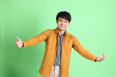 The young adult Asian man with smart casual clothes standing on the light green background.