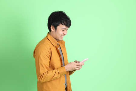 The young adult Asian man with smart casual clothes standing on the light green background.
