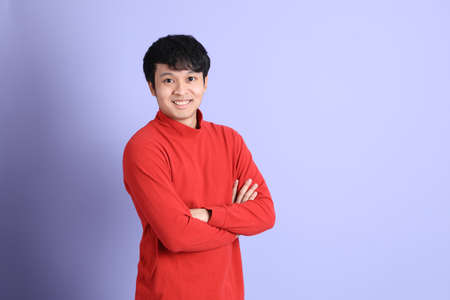 The young adult southeast Asian man with red long sleeve shirt standing on the light green...