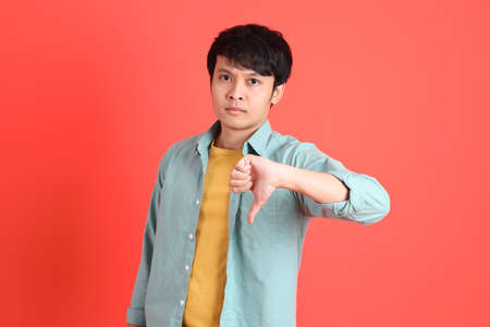 The young adult southeast Asian man with green shirt standing on the orange background.