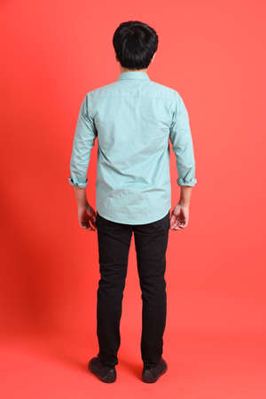 The young adult southeast Asian man with green shirt standing on the orange background.