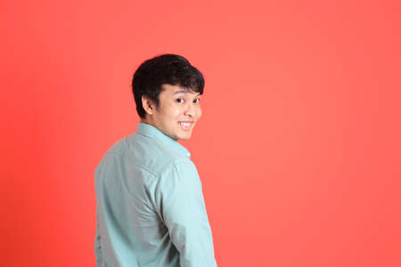 The young adult southeast Asian man with green shirt standing on the orange background.の写真素材