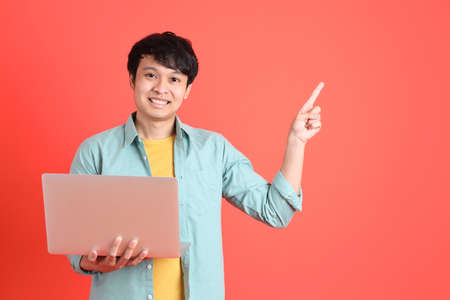 The young adult southeast Asian man with green shirt standing on the orange background.の写真素材