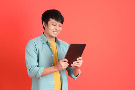 The young adult southeast Asian man with green shirt standing on the orange background.の写真素材