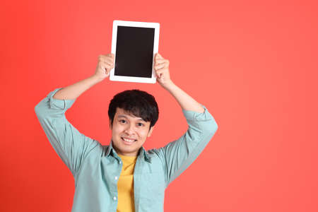 The young adult southeast Asian man with green shirt standing on the orange background.