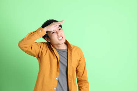 The young adult Asian man with smart casual clothes standing on the light green background.