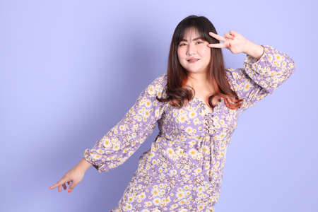 The chubby Asian woman standing on the purple background with the casual clothes.の写真素材