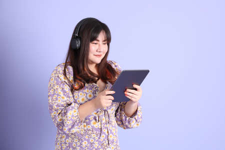 The chubby Asian woman standing on the purple background with the casual clothes.の写真素材