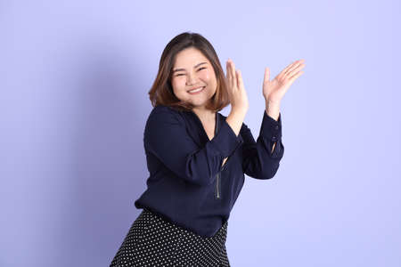 The chubby Asian woman standing on the purple background with the casual clothes.