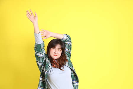 The chubby Asian woman standing on the yellow background with the casual clothes.