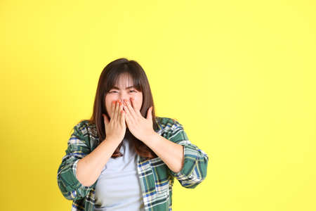 The chubby Asian woman standing on the yellow background with the casual clothes.の写真素材
