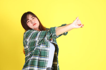 The chubby Asian woman standing on the yellow background with the casual clothes.の写真素材