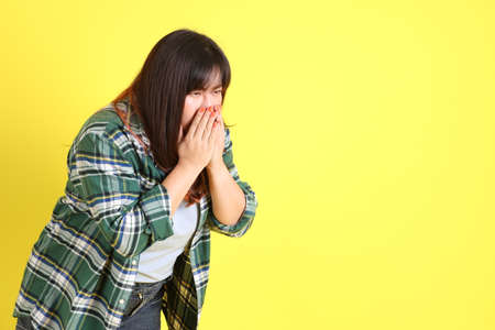 The chubby Asian woman standing on the yellow background with the casual clothes.