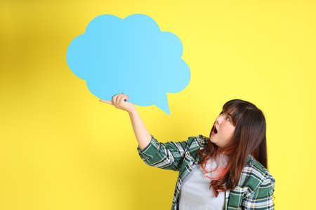 The chubby Asian woman standing on the yellow background with the casual clothes.