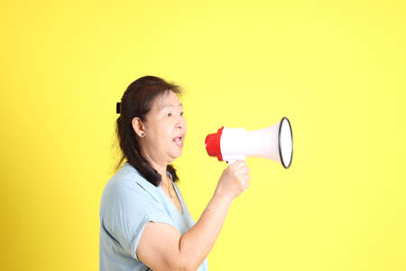 The Asian senior woman wearing light blue shirt standing on the yellow background.の写真素材