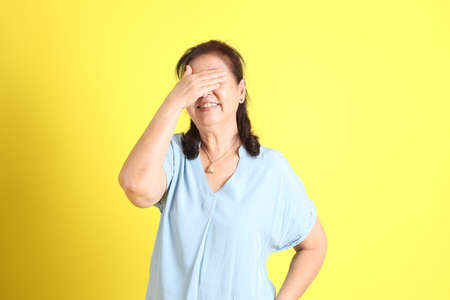 The Asian senior woman wearing light blue shirt standing on the yellow background.の写真素材