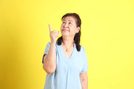 The Asian senior woman wearing light blue shirt standing on the yellow background.の写真素材